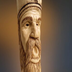 A carved face on a stick handle. Face is of a king-like character with crown, beard and mustache. Facial features are etched using a burning tool.