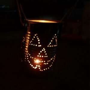A tin can painted black, with holes made in the shape of a smiley face with triangle eyes, through which light glows. Whole scene is dark to enhance the glowing face effect